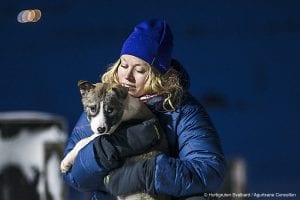 Blonde girl with dark blue beanie hat and puffer jacket holding sled dog puppy in Svalbard, Arctic Norway