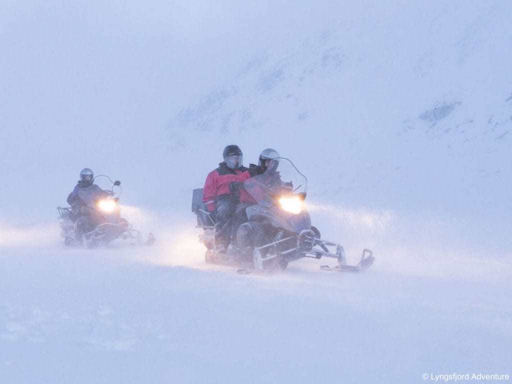 Two snowmobiles driving with lights on in foggy snow conditions in Lyngen, Arctic Norway