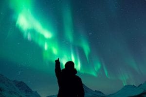 silhouette of person pointing at northern lights in tromso