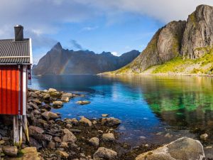 Eliassen Rorbuer in Lofoten Islands Norway with rainbow and mountain fjords and sea of water with rocks and red cabin